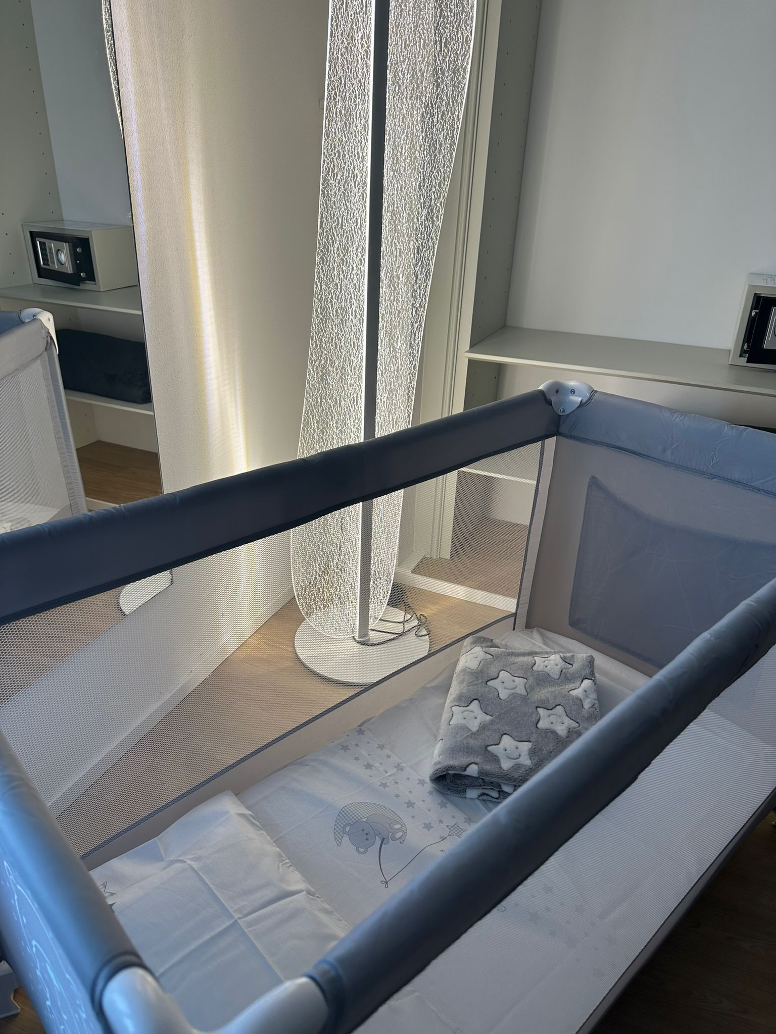 Ein Babybett mit einem Netz an der Seite, einer weichen Matratze und einem Kissen mit Sternenmuster.