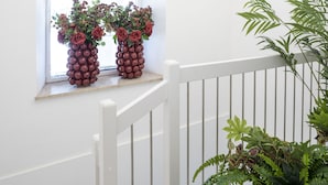 A staircase with white railings, a window with a view, and two potted plants with red flowers. - Le stanze del Savonarola  (Ferrara)