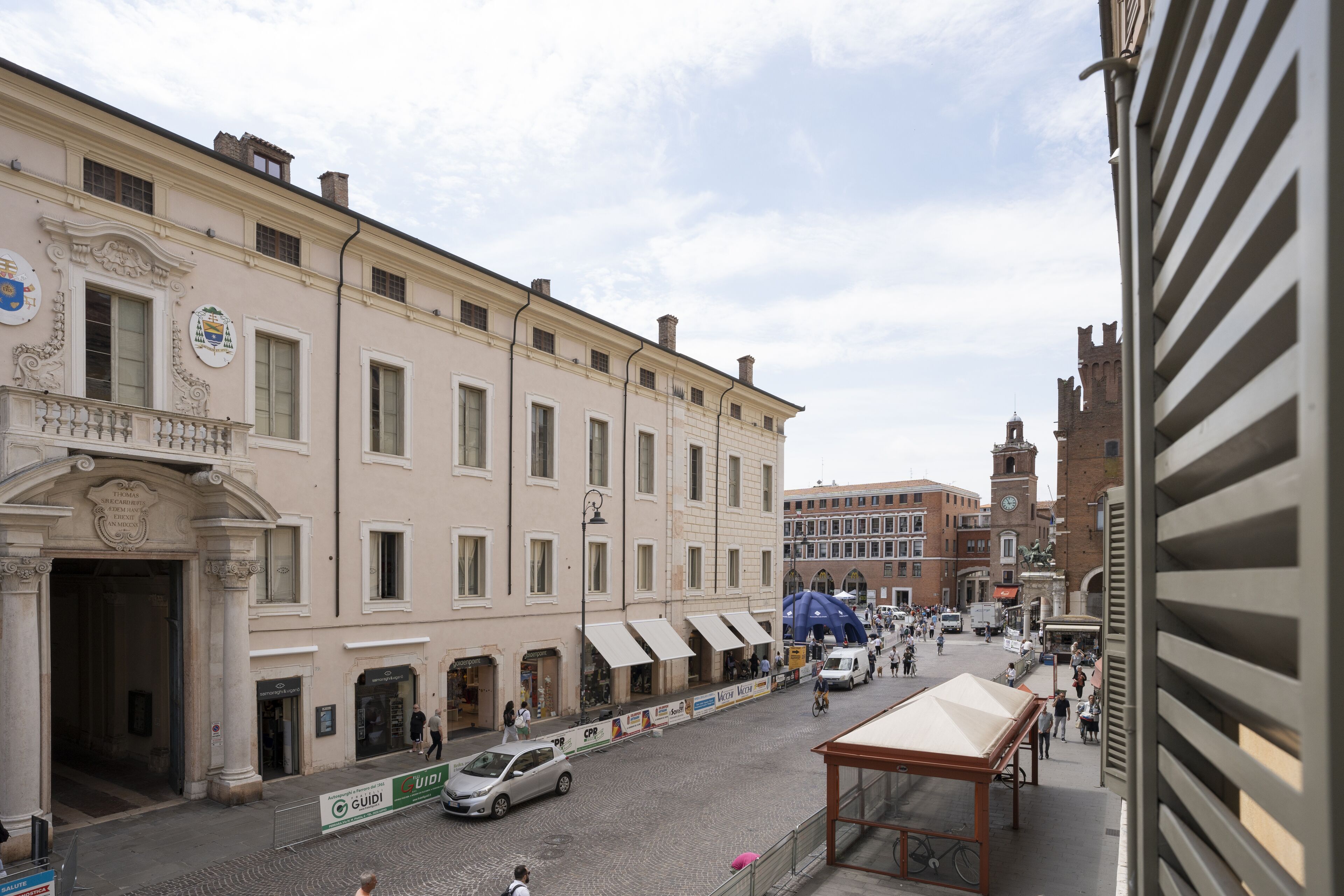 A street view with a building featuring a large entrance, multiple windows, and a clock tower in the background.