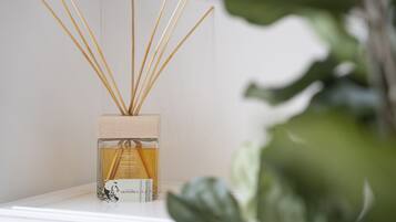Eine Parfumflasche mit Schilfstrohhalmen in einem klaren Glasbehälter auf weißer Oberfläche.