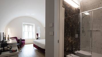 A modern bedroom with a large bed, a desk with a computer, and a chair. There is a bathroom with a shower and a toilet.