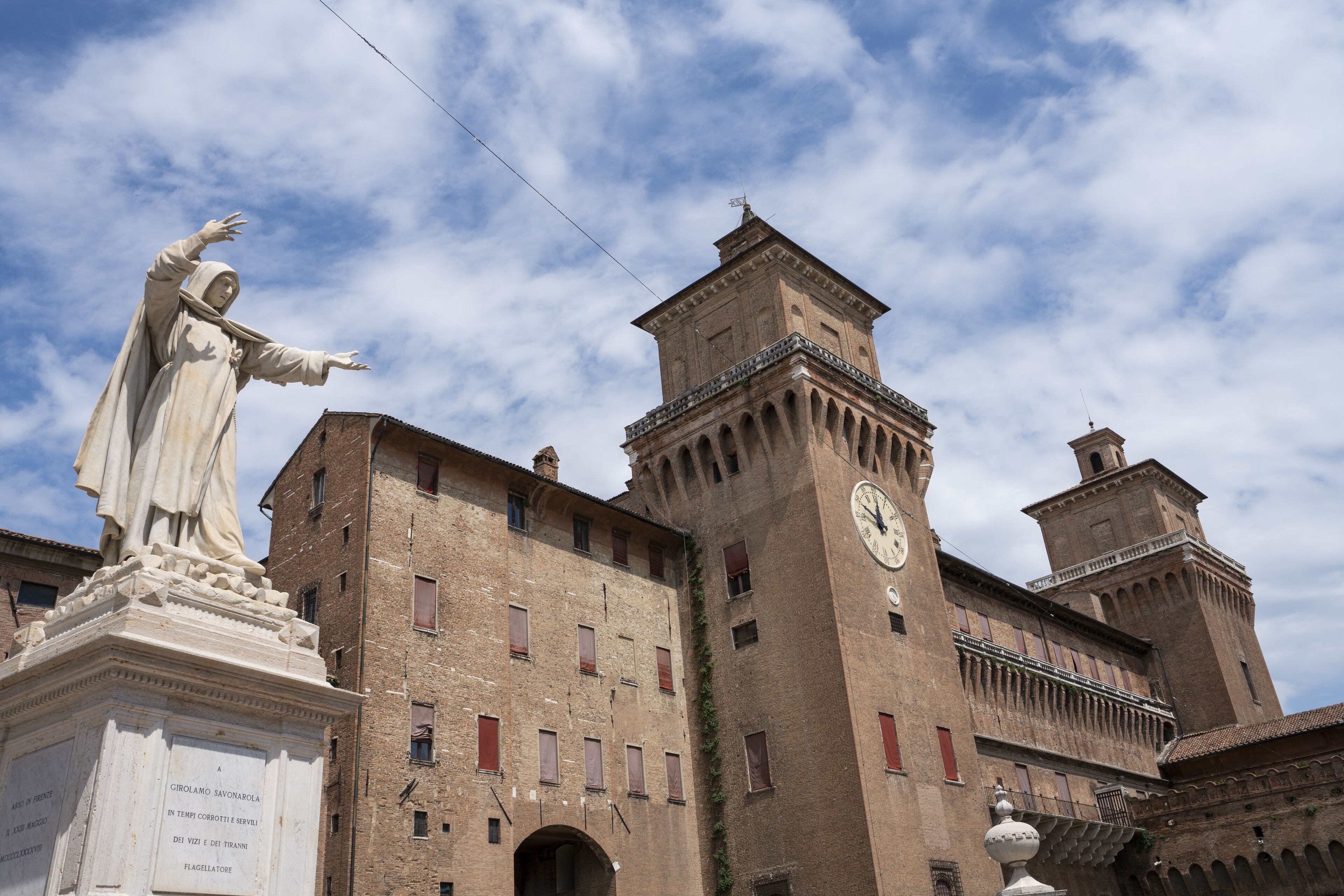 A historic building with a clock tower and a statue in front.
