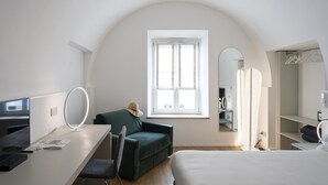A modern hotel room with a desk, chair, and a large bed. There is a window providing natural light, a mirror, and a wardrobe. - Le stanze del Savonarola  (Ferrara)