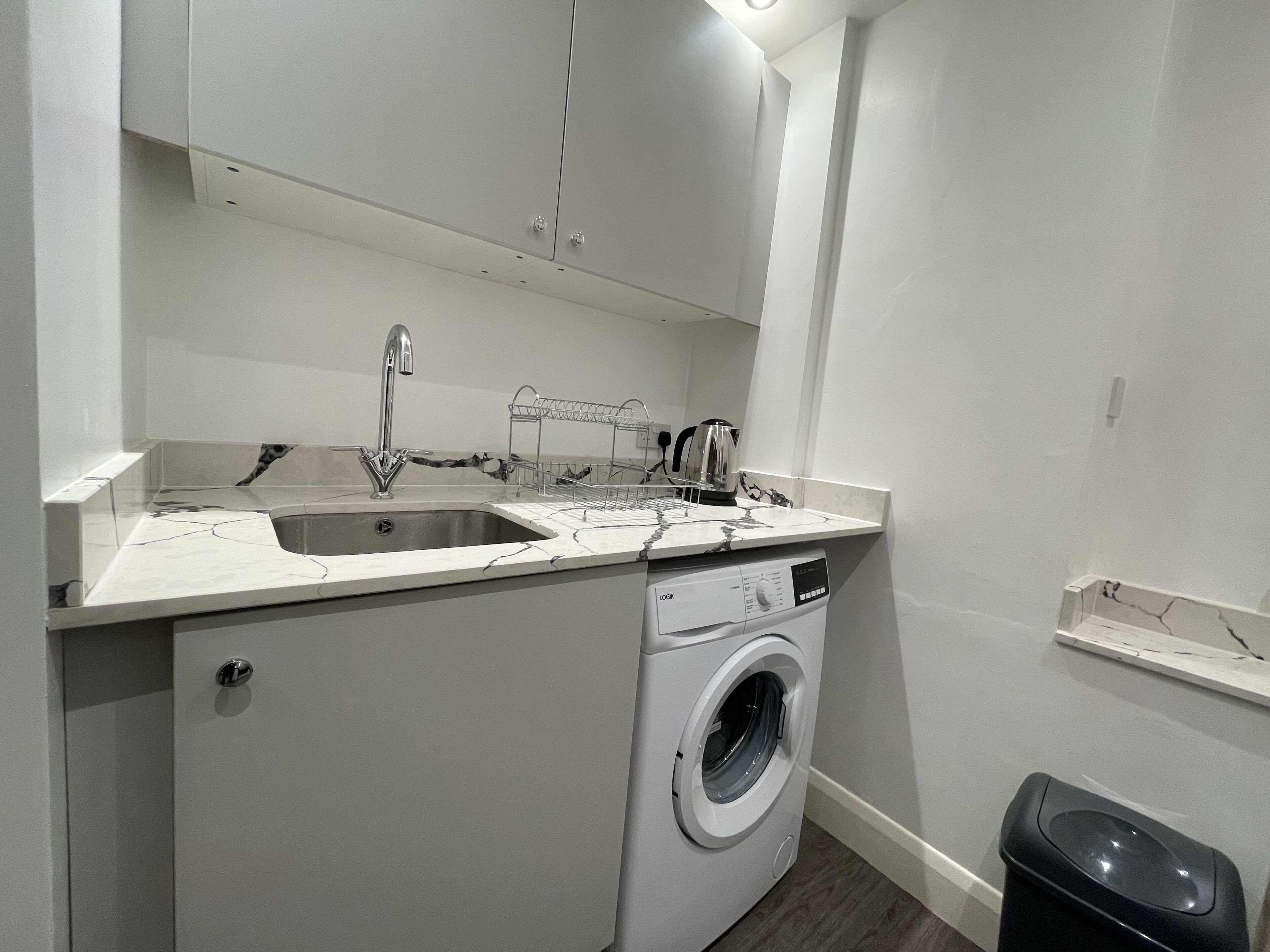 A compact laundry room with a washing machine, a sink, and a drying rack.