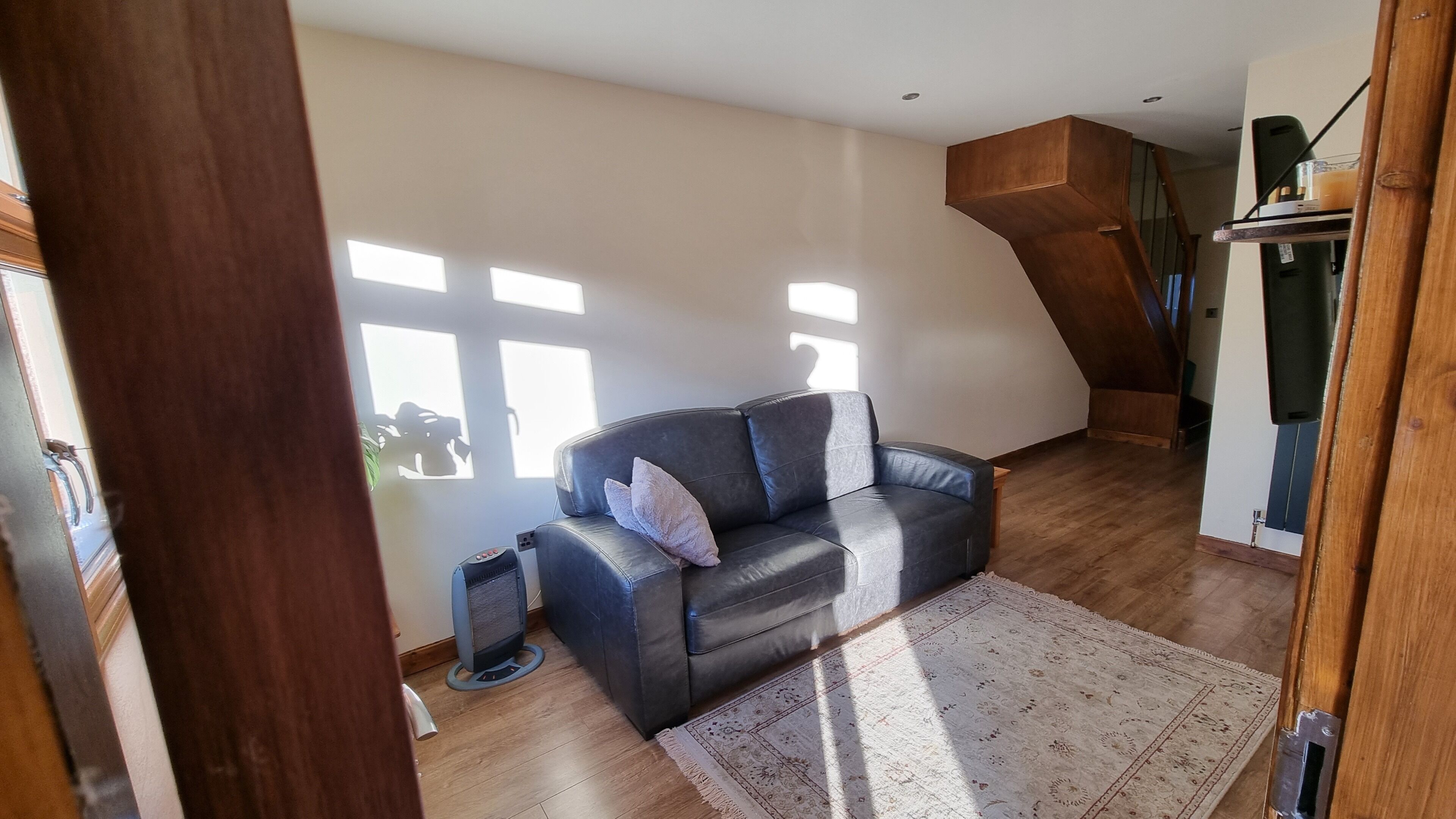 Un salón espacioso con un sofá de cuero negro, un tapete estampado y una escalera de madera.