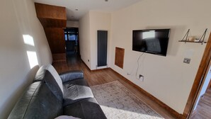 A living room with a sofa, a TV mounted on the wall, a radiator, and a wooden staircase. - Captivating 1-bed Apartment in Edinburgh (Edinburgh)