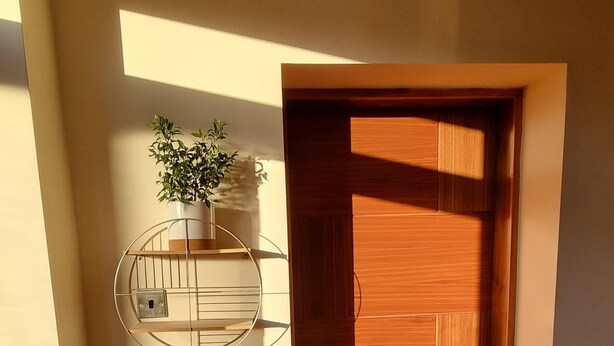 A hallway with a wooden door, a wall-mounted shelf with a plant, and a dark rug on the floor. - Captivating 1-bed Apartment in Edinburgh (Edinburgh)