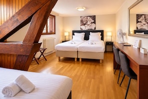Habitación de hotel con techo de madera, dos camas con sábanas blancas, un escritorio con silla, un radiador y un espejo grande.