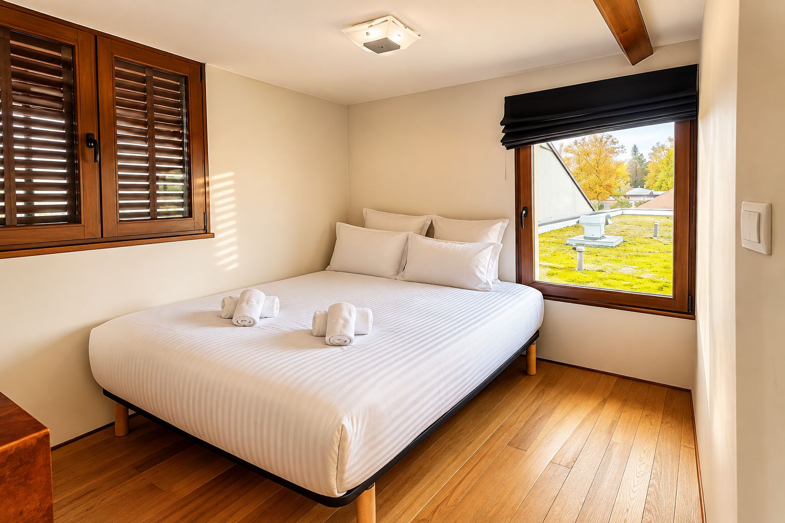 A bedroom with a bed, white linens, a window with a view of the outdoors, and wooden flooring.