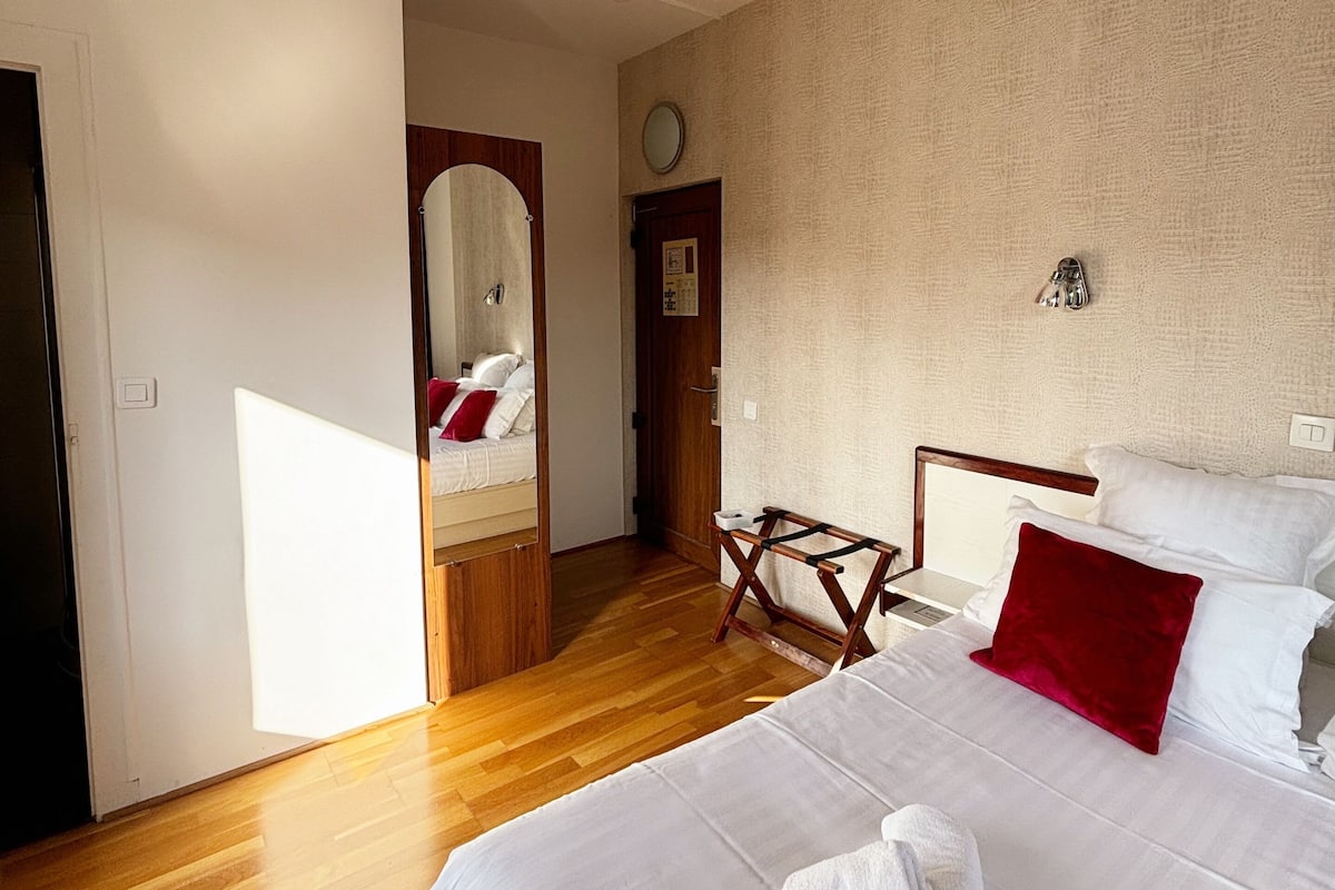 A hotel room with a large bed, wooden flooring, a wooden headboard, a bedside table, and a nightstand.