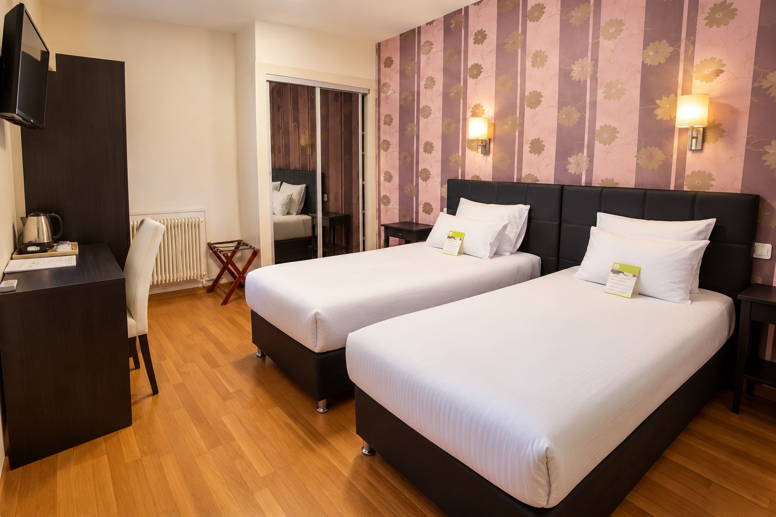 Ein Hotelzimmer mit zwei Betten, einem Schreibtisch, einem Heizkörper und einem Fernseher.