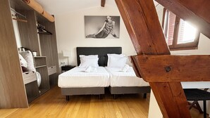 A bedroom with two beds, wooden flooring, a loft-style ceiling, and a large window. - Le Divona (Divonne-les-Bains)