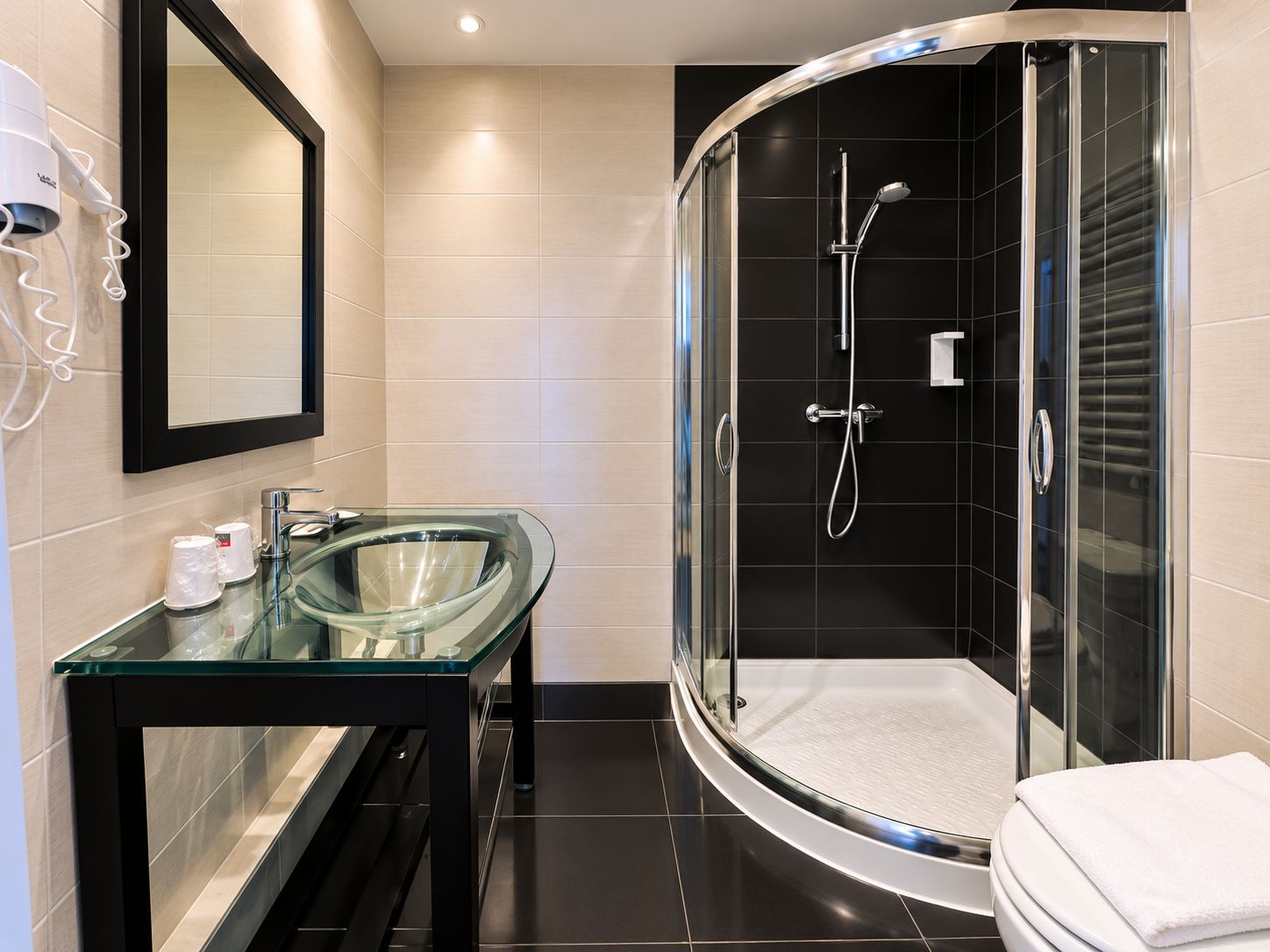 A modern bathroom with a glass-enclosed shower, a glass sink, and a black-framed mirror.