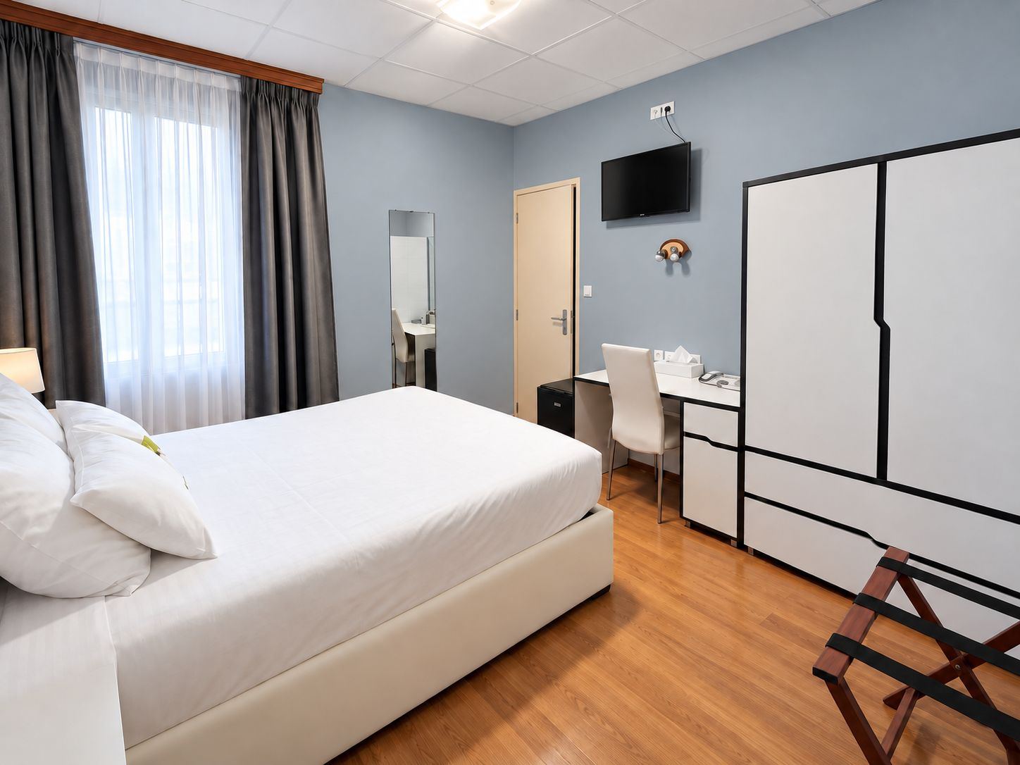 A hotel room with a bed, a desk, a chair, a television, and a wardrobe.