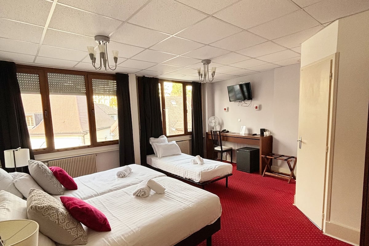 A hotel room with two beds, a desk, a chair, a TV, and a window with curtains.