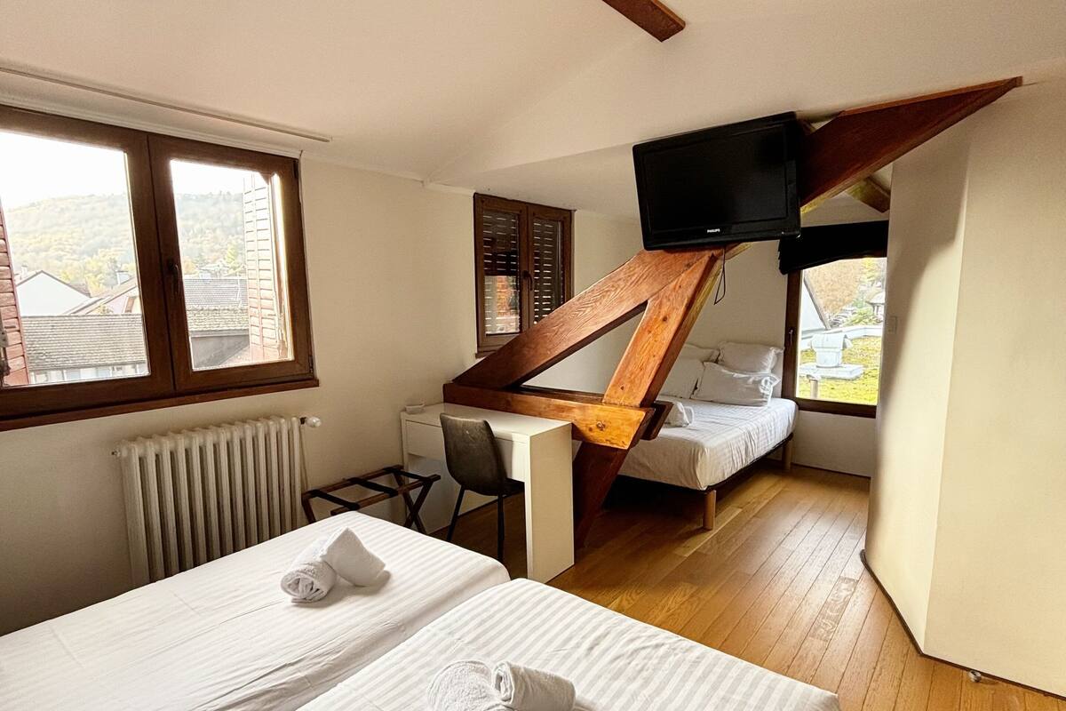 A hotel room with two beds, a desk, a television, and a view of the outside.