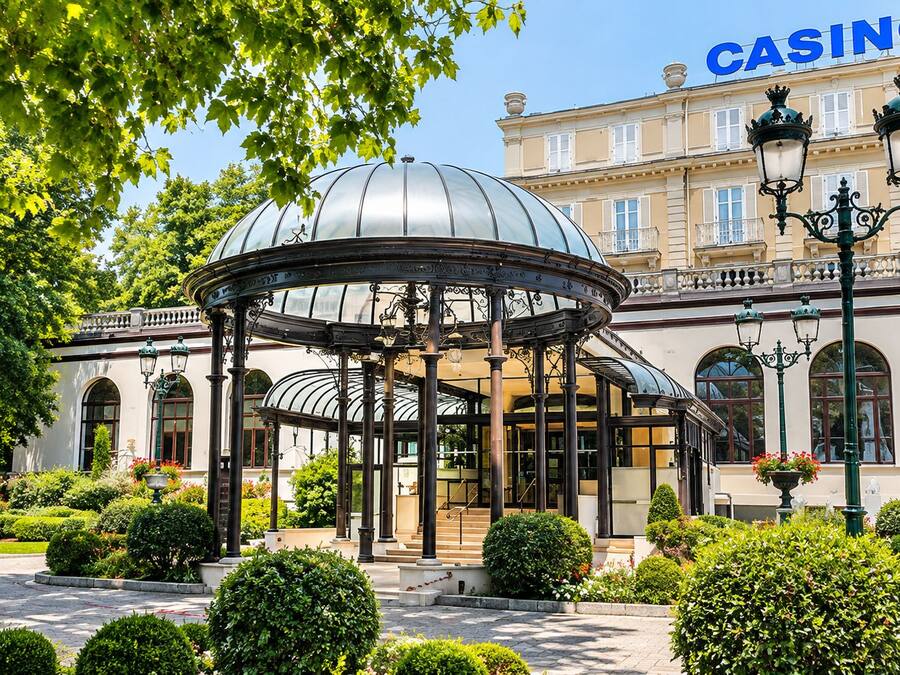 Área externa coberta com estrutura em cúpula, cercada por sebes bem cuidadas e um edifício com a placa 'CASINO'.