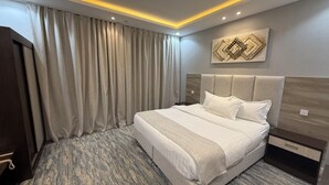 A hotel room with a large bed, a headboard, a wall-mounted artwork, and a curtain. - Qimam Park Hotel 2 Abha (Abha)