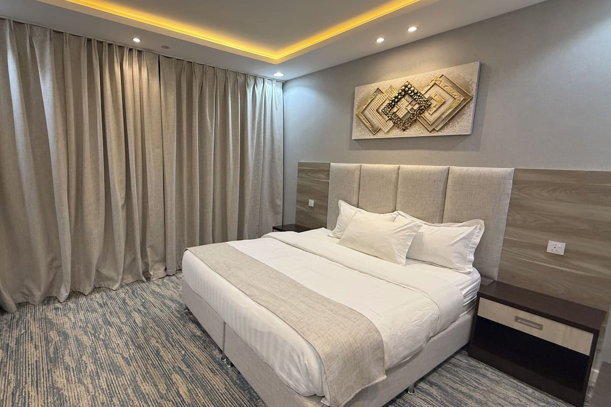 A hotel room with a large bed, a headboard, a wall-mounted artwork, and a curtain.