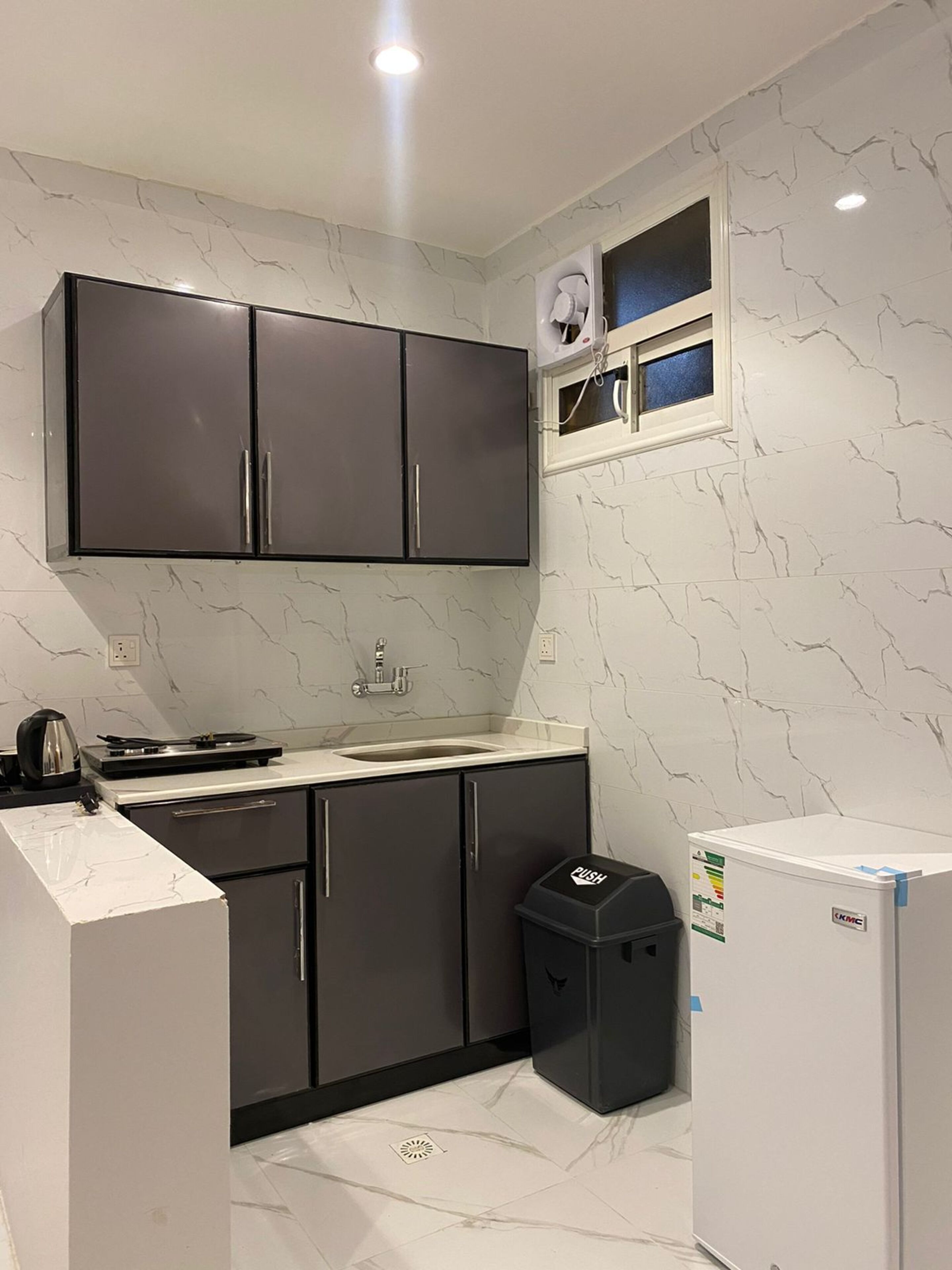 Una cocina compacta con armarios oscuros, una encimera blanca, un lavabo, una estufa y un ventanal pequeño.