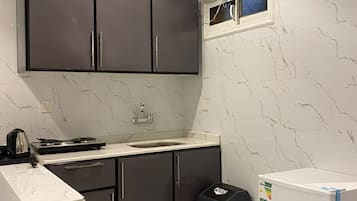 Una cocina compacta con armarios oscuros, una encimera blanca, un lavabo, una estufa y un ventanal pequeño.
