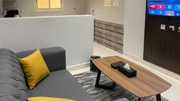 A modern living room with a grey sofa, a wooden coffee table, and a flat-screen TV mounted on the wall. - Qimam Park Hotel 2 Abha (Abha)