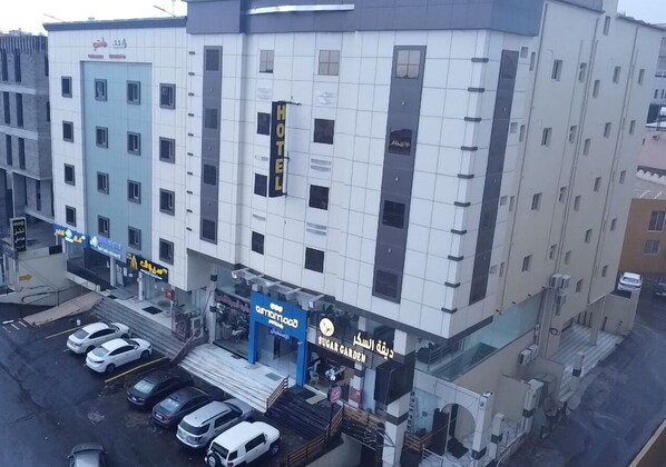 Monikerroksinen hotelli, jossa on moderni julkisivu ja sen edessä suuri, selkeästi näkyvä «HOTEL»-kyltti. Edessä on useita parkkeerattuja autoja, ja alakerrassa näkyy «SUGAR GARDEN» -kyltti.