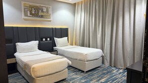 Hotellihuone, jossa on kaksi sänkyä, sängynpääty, seinään kiinnitetty valaisin ja suuri ikkuna, jossa on verhot.