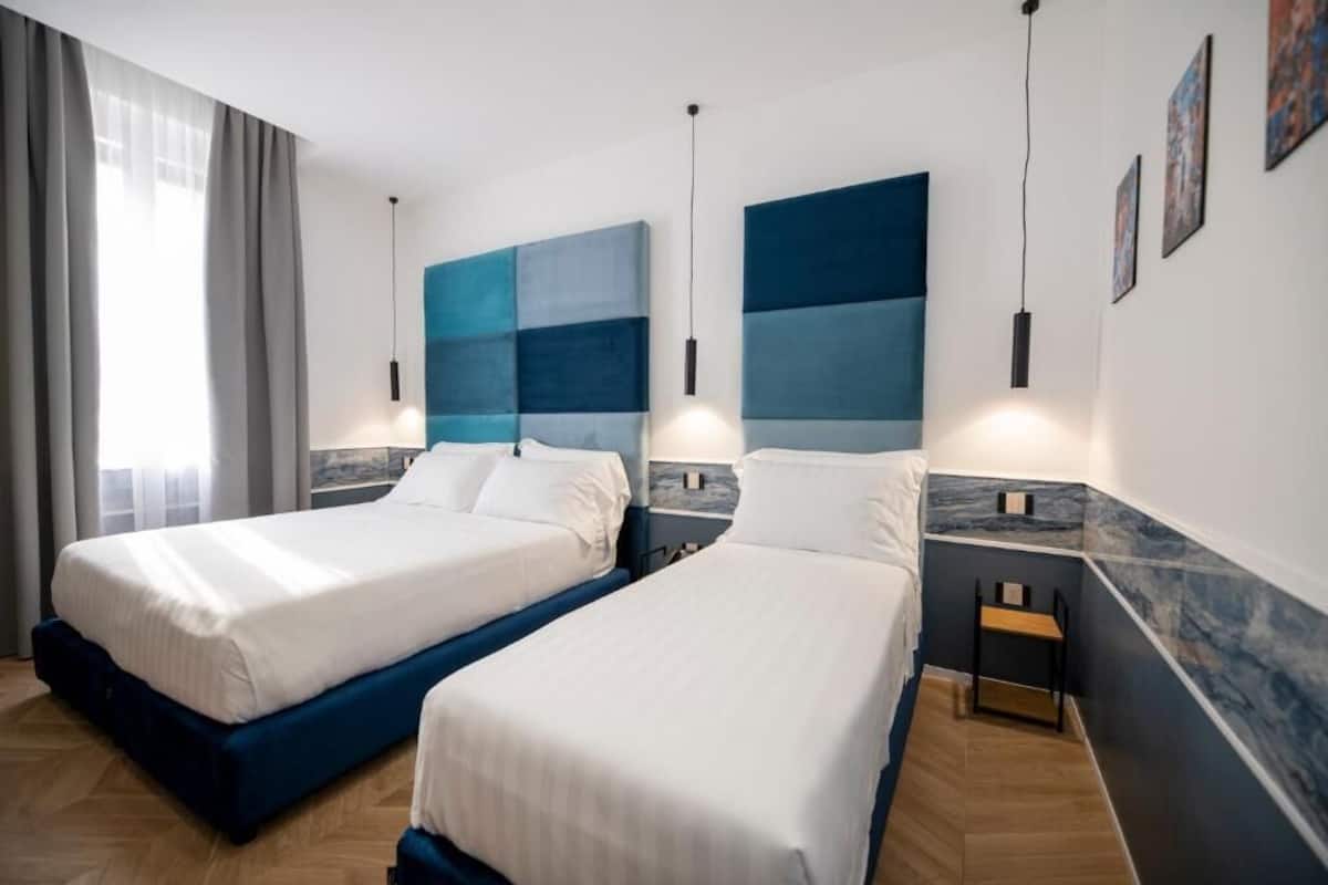 Ein Hotelzimmer mit zwei Betten, einer Wand mit Marmorverkleidung und Kunstwerken an der Wand.