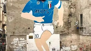 Une personne portant un maillot de sport bleu avec le numéro 10, debout devant un mur texturé orné de fenêtres et de climatiseurs.