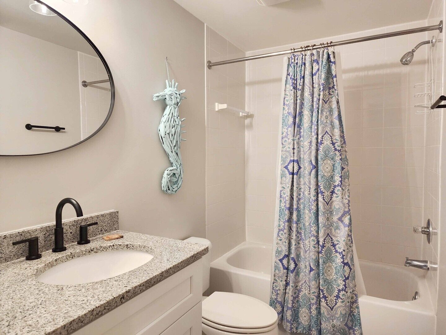 Ein Badezimmer mit einem Granitwaschbecken, einer Toilette, einer Dusche mit gemustertem Vorhang und einem Handtuchhalter an der Wand.