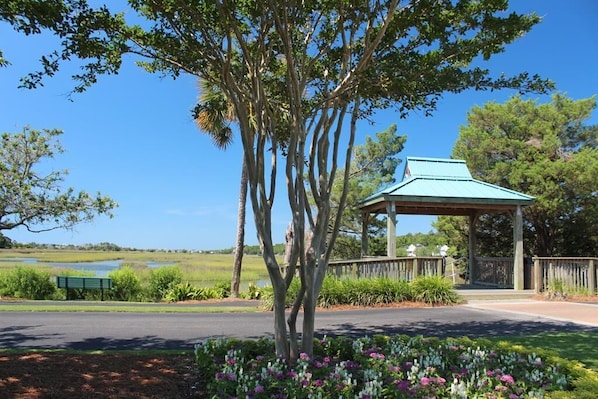 A gazebo with a green roof, surrounded by a wooden fence, near a body of water and a road.