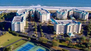 A coastal hotel complex with multiple buildings, a tennis court, and a beach view.