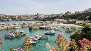Un pueblo costero con un puerto deportivo lleno de barcos, una playa de arena y edificios al fondo.