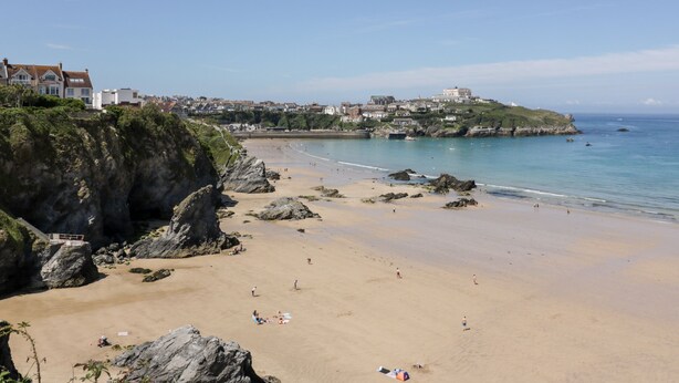 Una playa costera con costas rocosas, una playa de arena y edificios al fondo.
