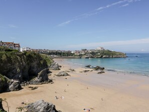 Une plage côtière aux rivages rocheux, avec une partie sablonneuse et des bâtiments visibles à l’arrière-plan.