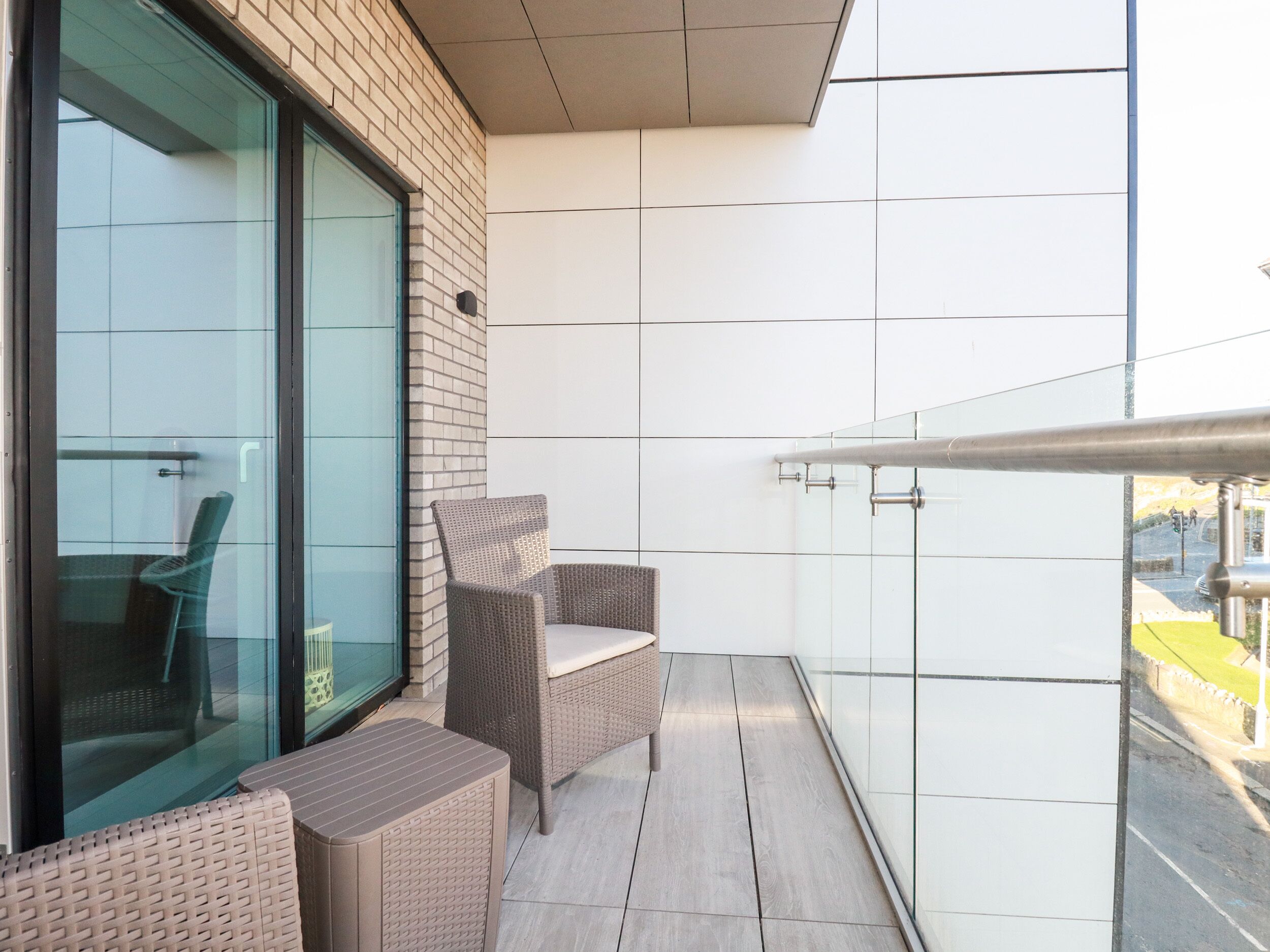 A balcony with wicker furniture, a glass door, and a view of the street.