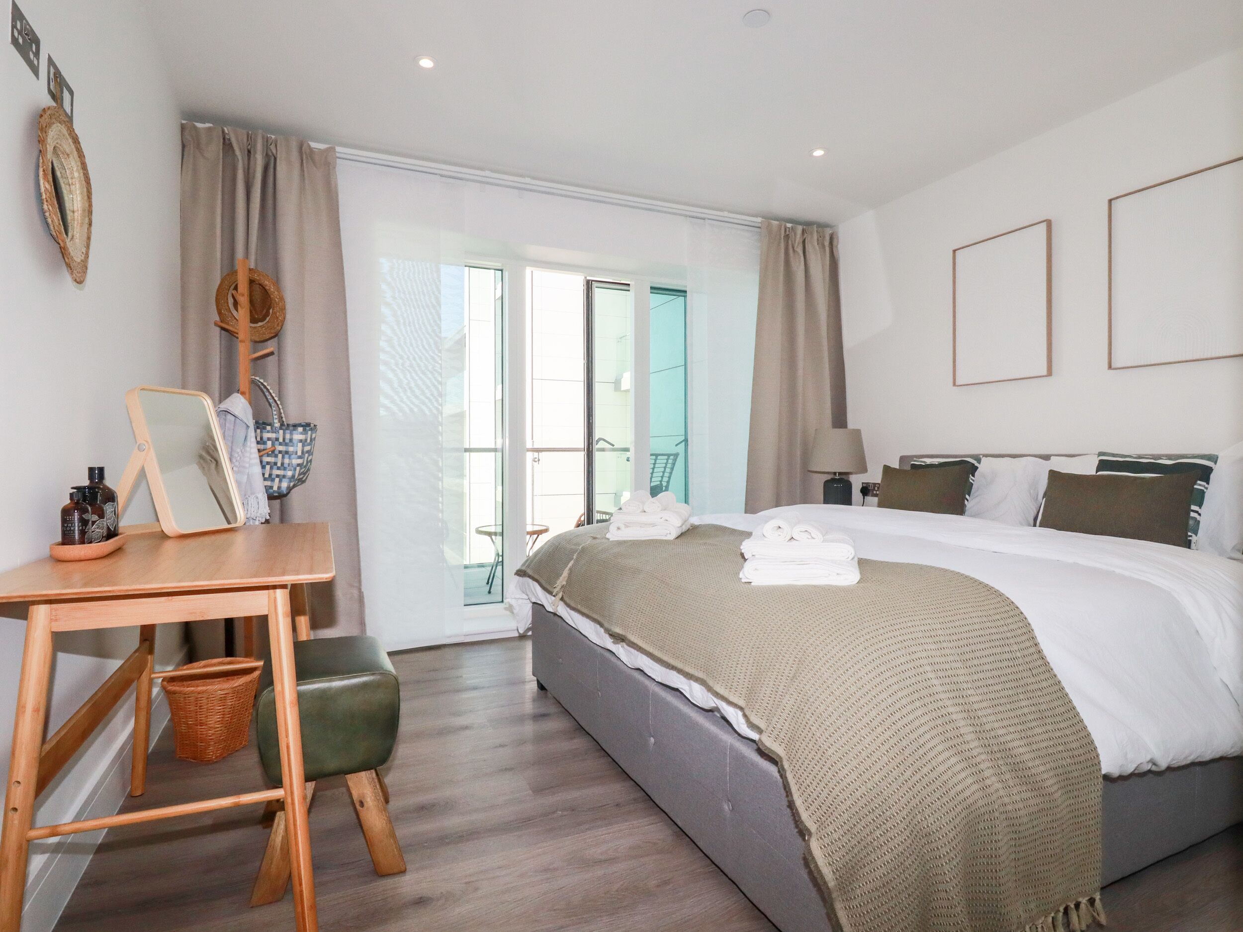 Une chambre d’hôtel comprenant un lit, un bureau, une chaise, une petite table, un miroir, une lampe et un balcon avec une chaise.