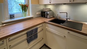 A modern kitchen with white cabinets, a wooden countertop, a built-in microwave, and a window with a view of greenery. - Cozy vacation home at the foot of the Hoher Meißner (Meißner)