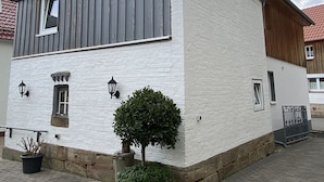 A white building with a gabled roof, a small window, and a potted plant in front. - Cozy vacation home at the foot of the Hoher Meißner (Meißner)
