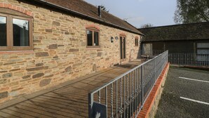 A stone building with a wooden deck and metal railing. - Cinder Cottage (Worcester)