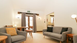 A modern living room with two grey sofas, a wooden coffee table, and a dining table with chairs. There is a kitchen area visible through an open door. - Cinder Cottage (Worcester)