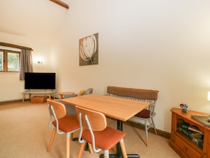 A cozy living room with a wooden dining table, two chairs, a bench, a television, and a bookshelf.