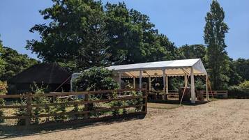 Un cadre extérieur rustique agrémenté d’une clôture en bois, d’un pavillon couvert et d’un sol en terre battue.