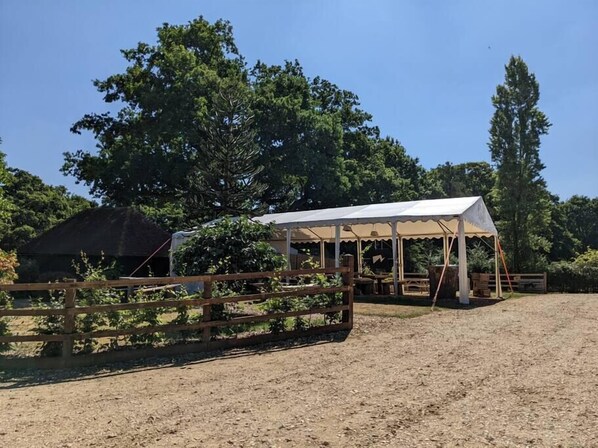 A rustic outdoor setting with a wooden fence, a covered pavilion, and a dirt ground.