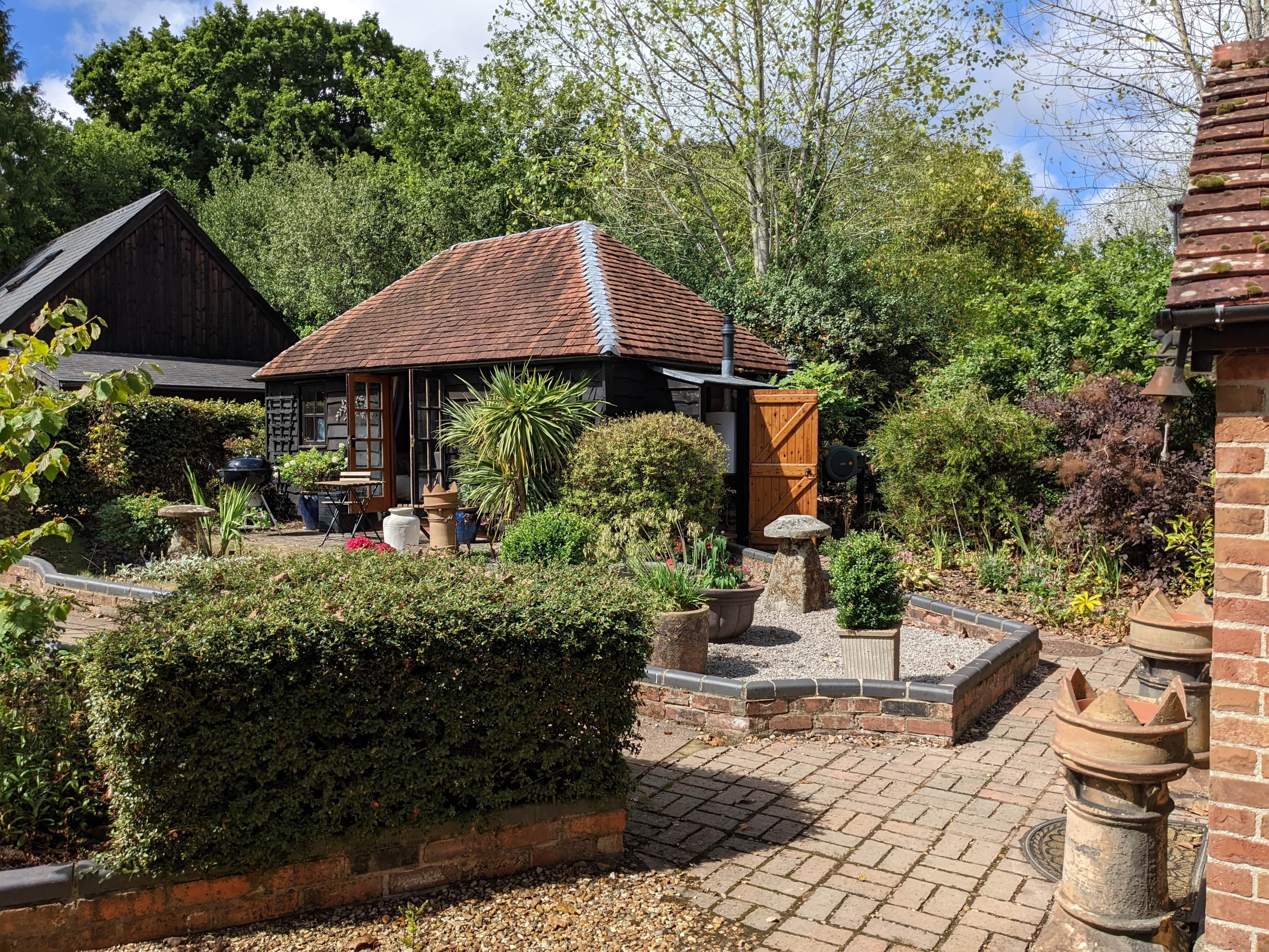 A rustic building with a tiled roof, surrounded by a well-maintained garden with various plants and a brick pathway.