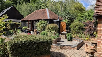 A rustic building with a tiled roof, surrounded by a well-maintained garden with various plants and a brick pathway.