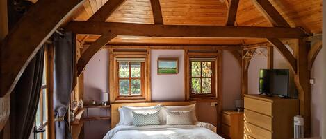 A bedroom with a wooden ceiling, a bed, a dresser, a television, and two windows with blinds.