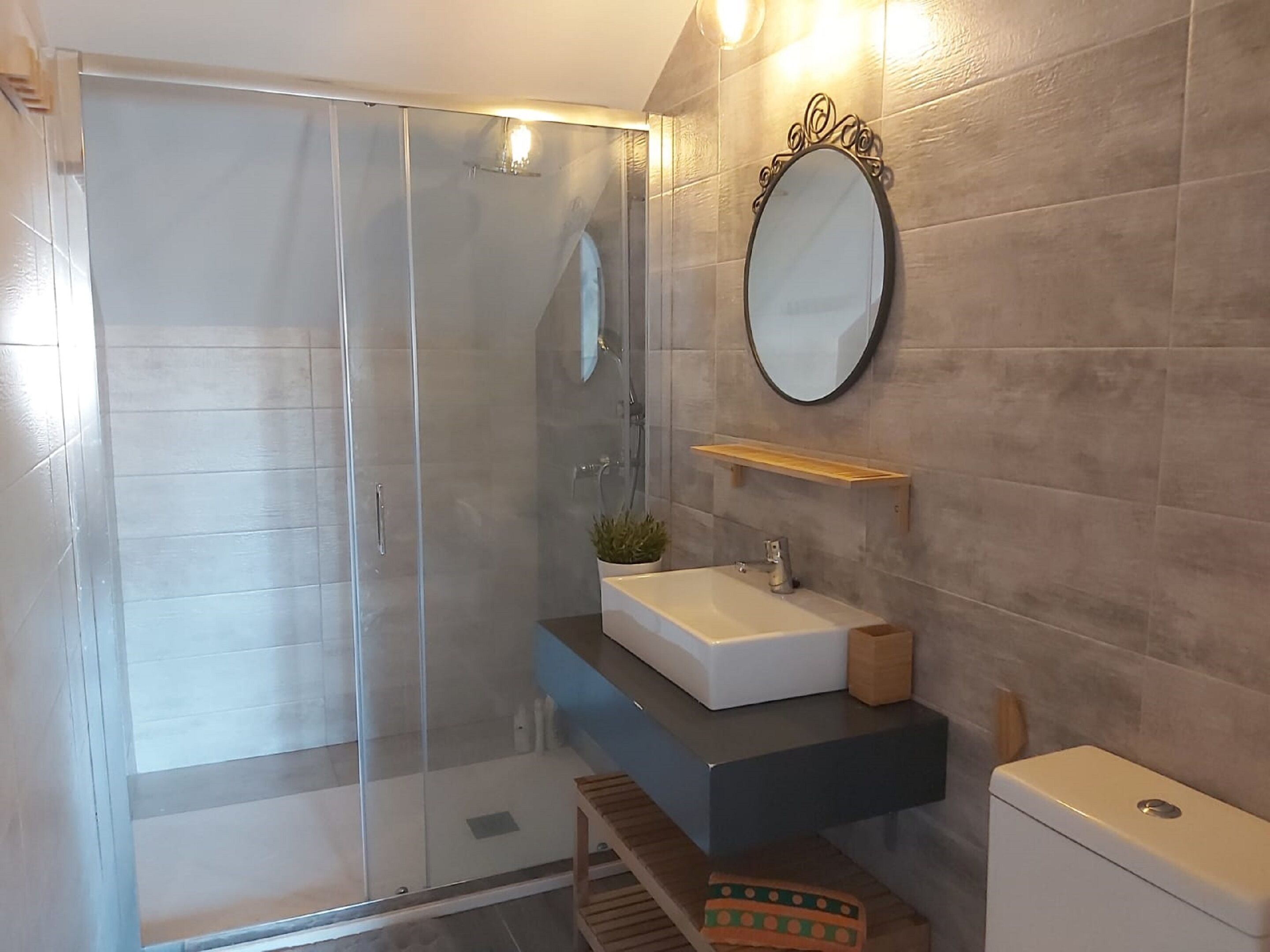 Une salle de bain moderne avec une douche à parois de verre, un lavabo blanc, un miroir doté d’un cadre orné et une étagère en bois.