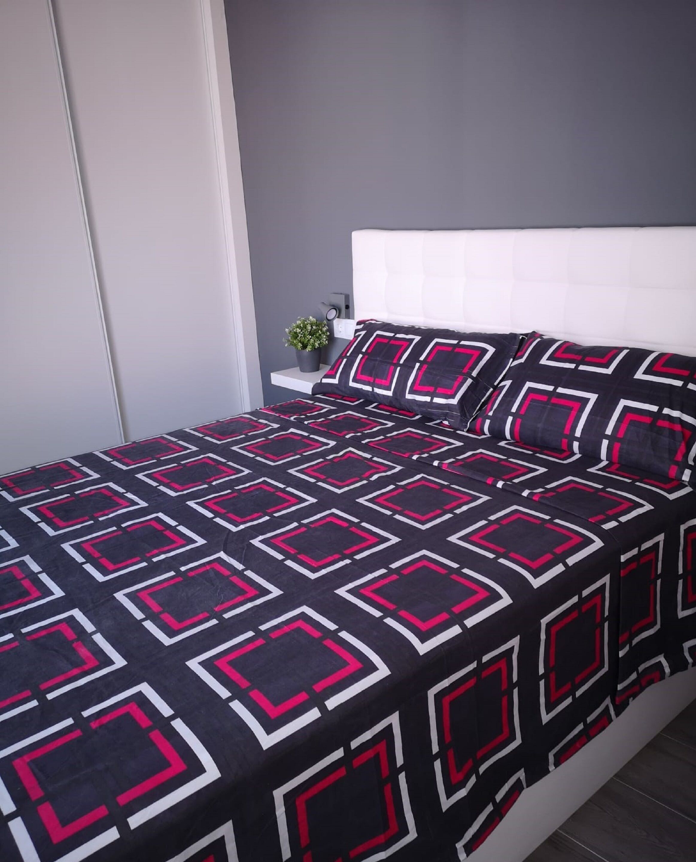 A bedroom with a bed, a nightstand, a potted plant, and a grey wall.